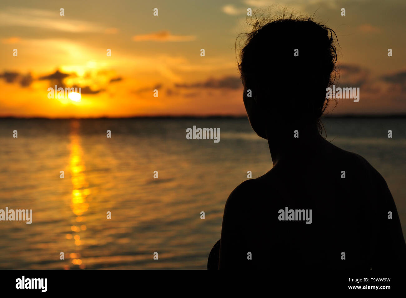 Una giovane donna orologi il tramonto dalla riva di tabacco Caye Belize Foto Stock