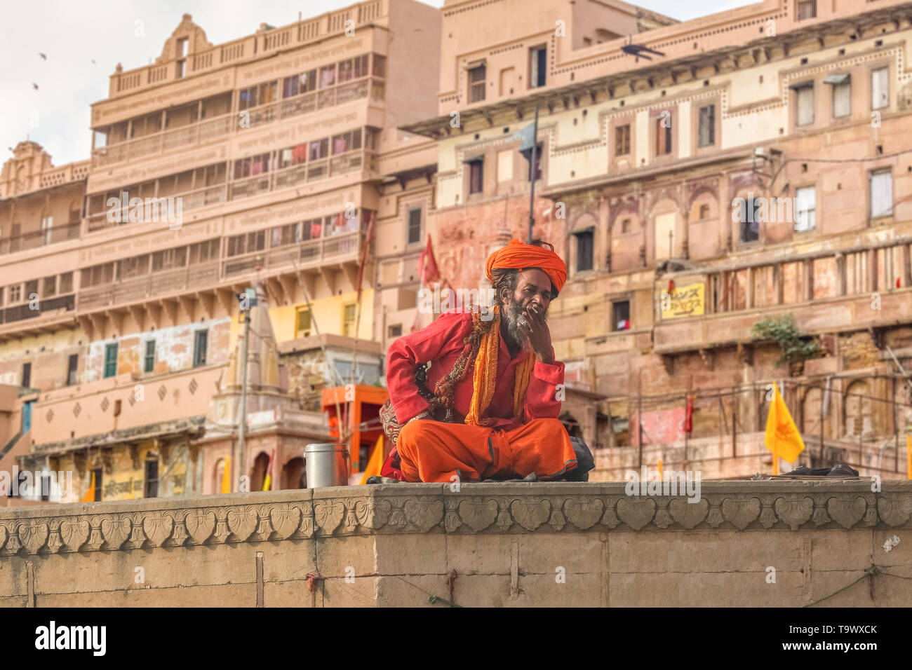 Sadhu baba seduta a Varanasi Gange ghat con architettura antica costruzione presso il fondale. Foto Stock