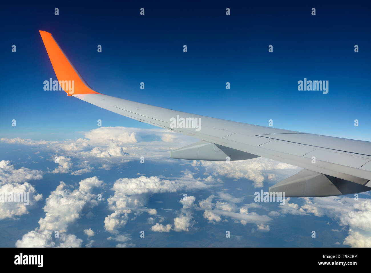 Ala di un aeroplano che vola al di sopra delle nuvole bianche in un cielo blu Foto Stock