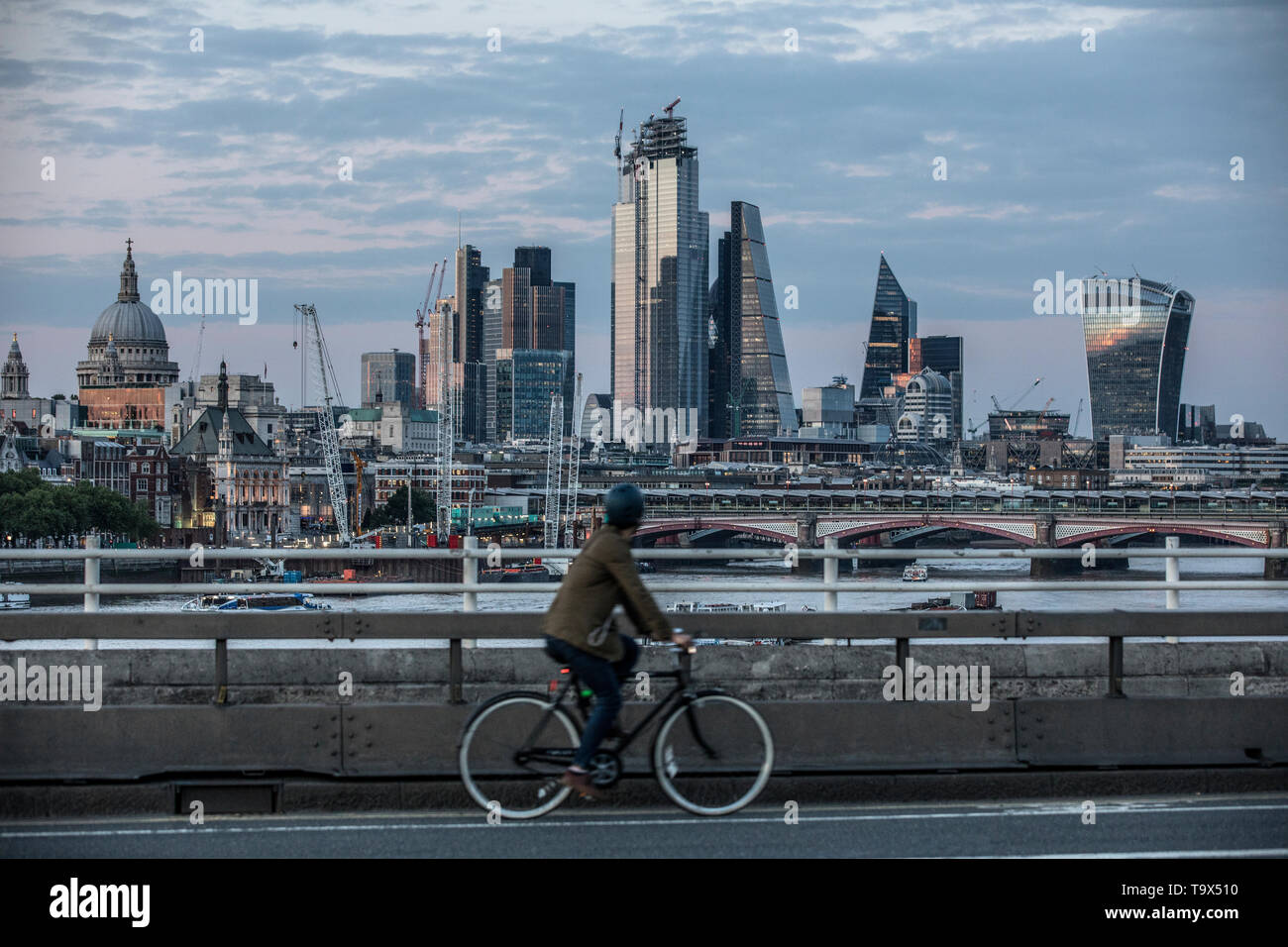 Ciclista attraversa il ponte di Waterloo con la Cattedrale di St Paul e i grattacieli della City Of London financial district in distanza, London, Regno Unito Foto Stock