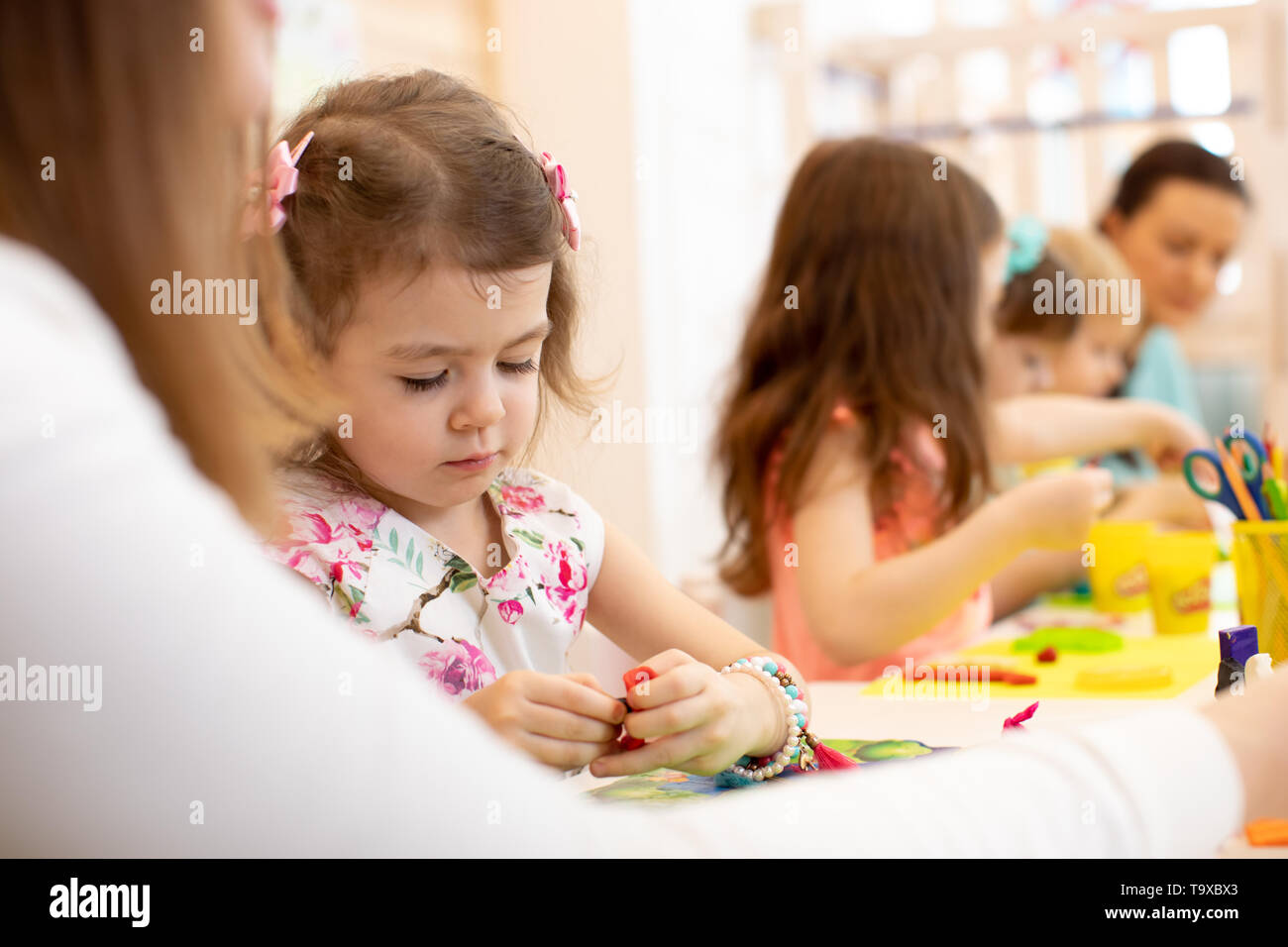 Un gruppo di bambini con gli insegnanti nella scuola materna. Bambini creare mestieri fuori di carta colorata. Foto Stock