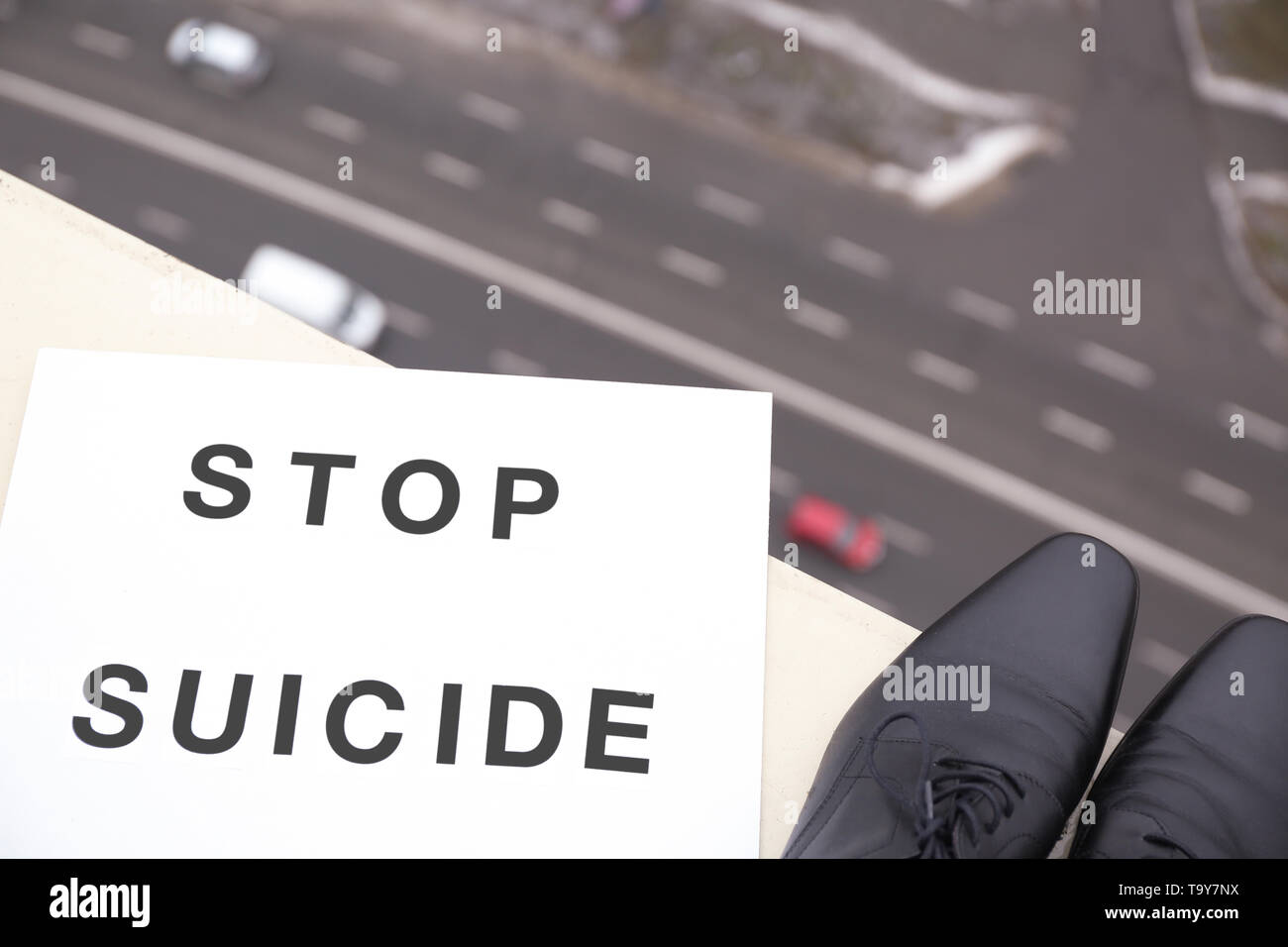 Scarpe maschio ed il foglio di carta con il testo STOP suicidio sul bordo del tetto Foto Stock