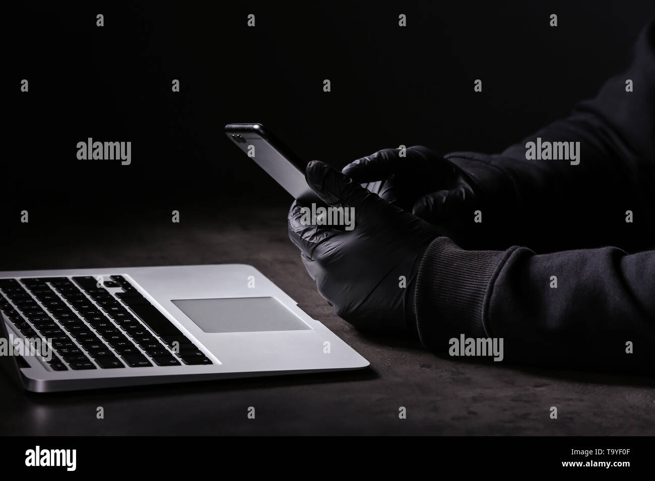 Professional hacker con il computer portatile e il telefono cellulare seduta a tavola su sfondo scuro Foto Stock