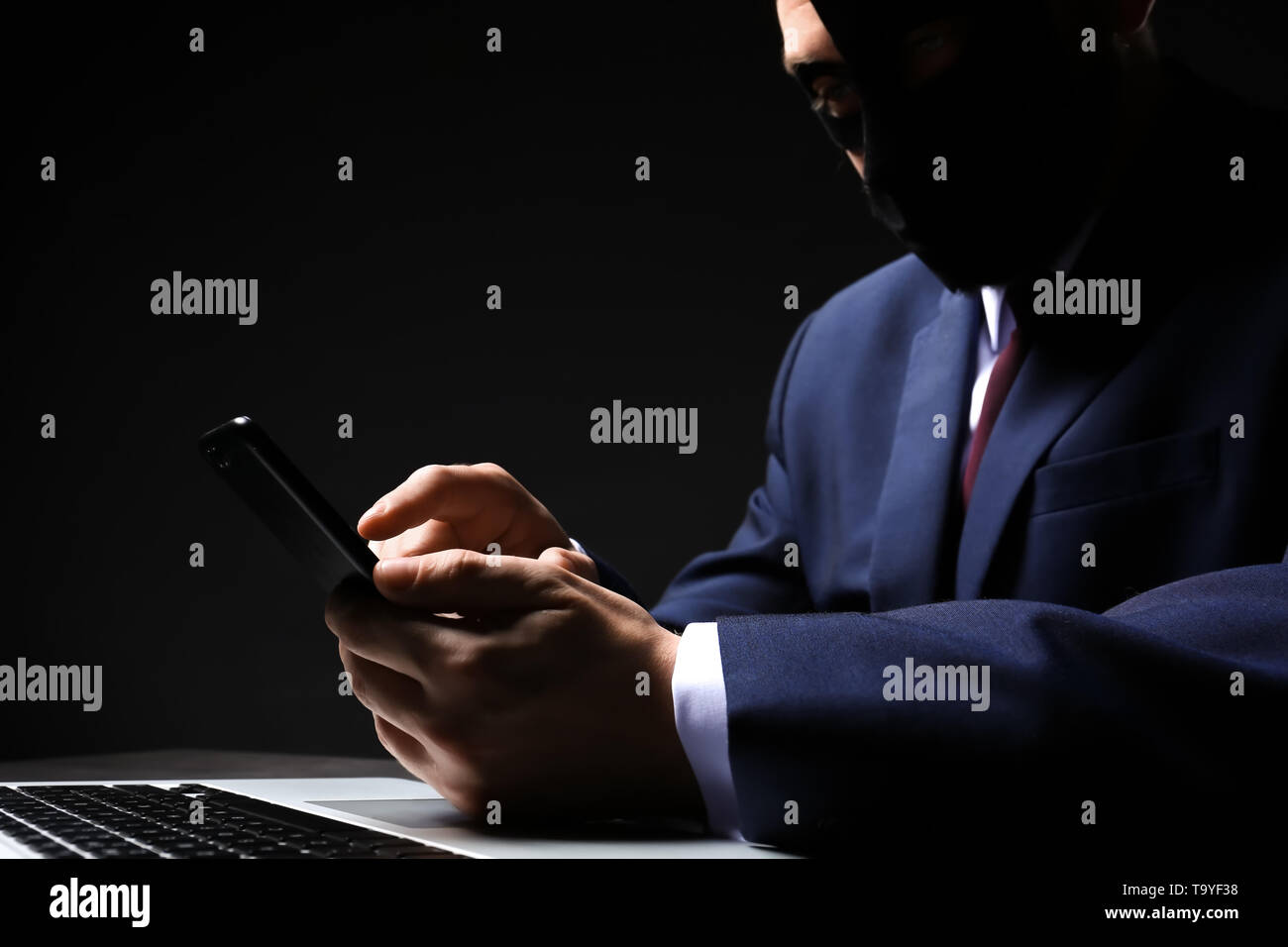 Professional hacker con il computer portatile e il telefono cellulare seduta a tavola su sfondo scuro Foto Stock