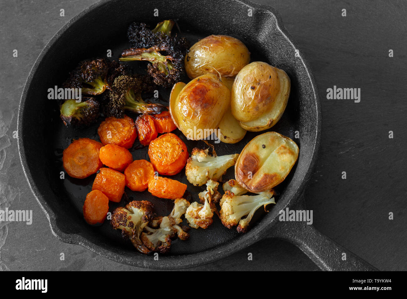 Arrosto di verdure fritte in una ghisa padella con patate, cavolfiore, carota e i broccoli. Su uno sfondo di ardesia. Foto Stock
