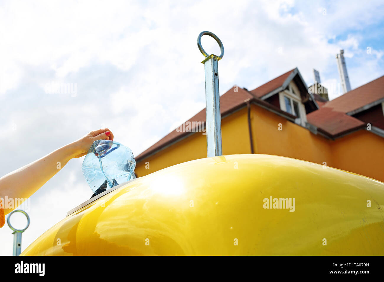 Riciclaggio di una donna getta rifiuti di plastica in un contenitore giallo Foto Stock