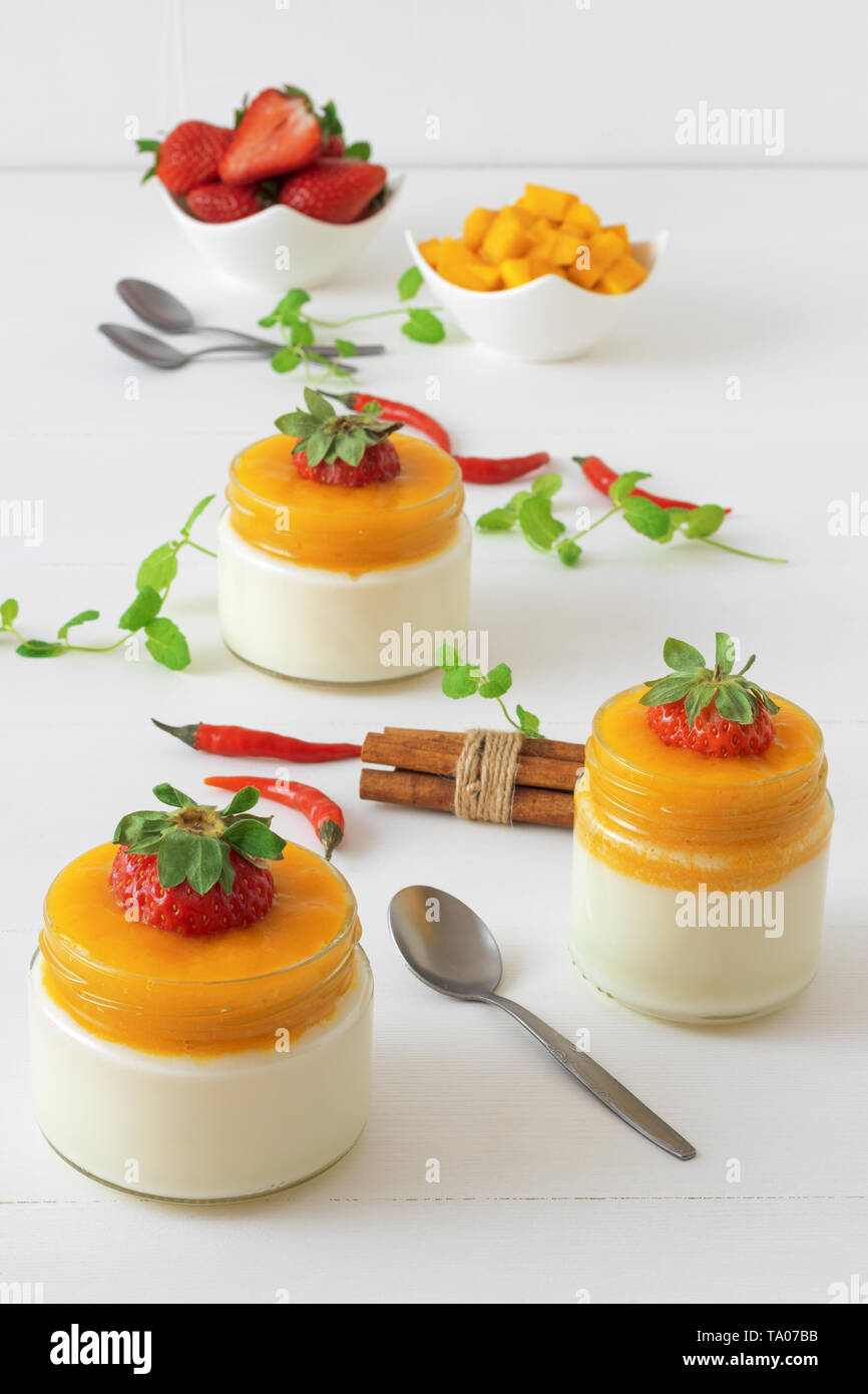 Italiano tradizionale dolce con Panna cotta con gelatina di mango con tocco di red hot chili Piri-Piri servita in vasi su bianco tavolo in legno e embellis Foto Stock