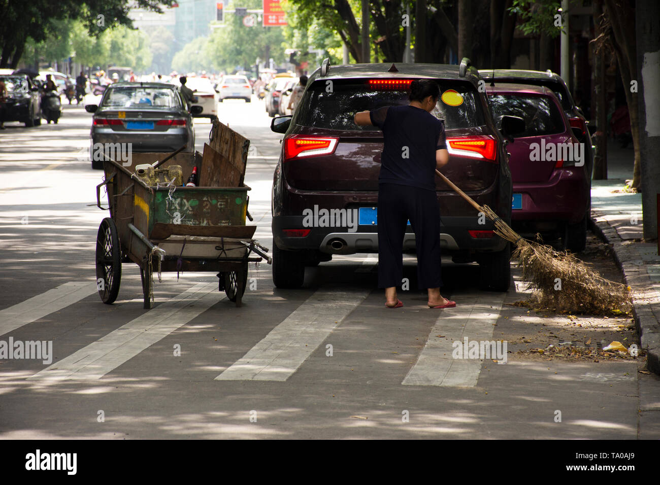 Donna cinese spazzatrice stradale lavorando pulire e mantenere la spazzatura e spingere il carrello di spazzatura in strada e la gente a piedi con il traffico a Teochew City il 8 maggio Foto Stock