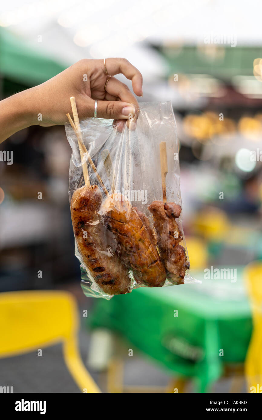 Sai Ua, la Northen thai salsiccia in mano della ragazza in un tipico sacchetto di plastica su alcuni bastoni di legno, Thailandia Foto Stock