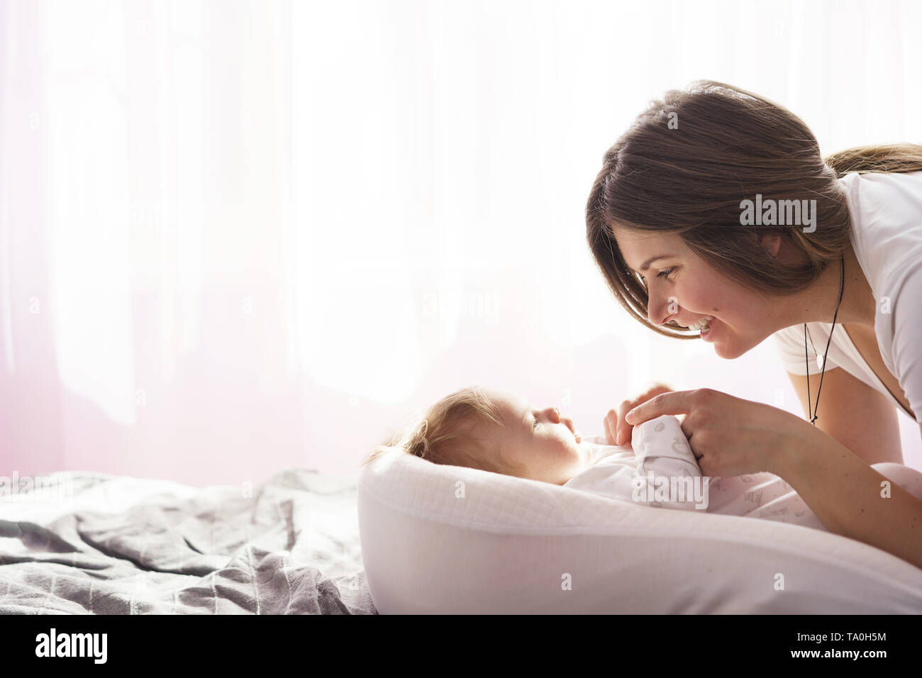 La madre con il figlio neonato sdraiato sul letto in i raggi di luce del sole proveniente dalla finestra Foto Stock