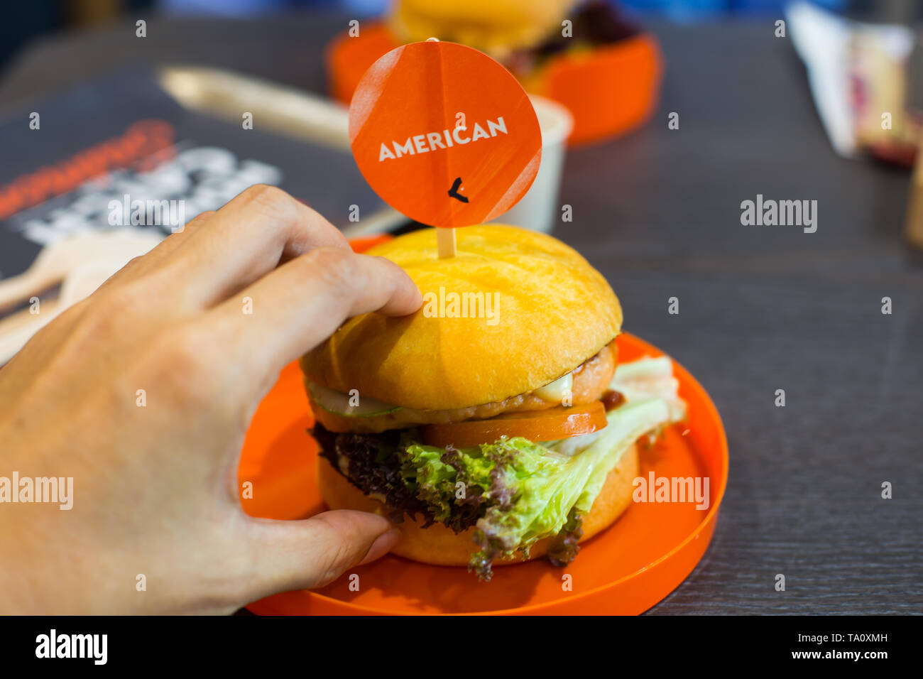 Prospettiva alternativa di una mano sinistra afferra un salmone norvegese burger da orange la piastra di plastica. Foto Stock Prospettiva alternativa di una mano sinistra afferra un salmone norvegese burger da orange la piastra di plastica. Foto Stock