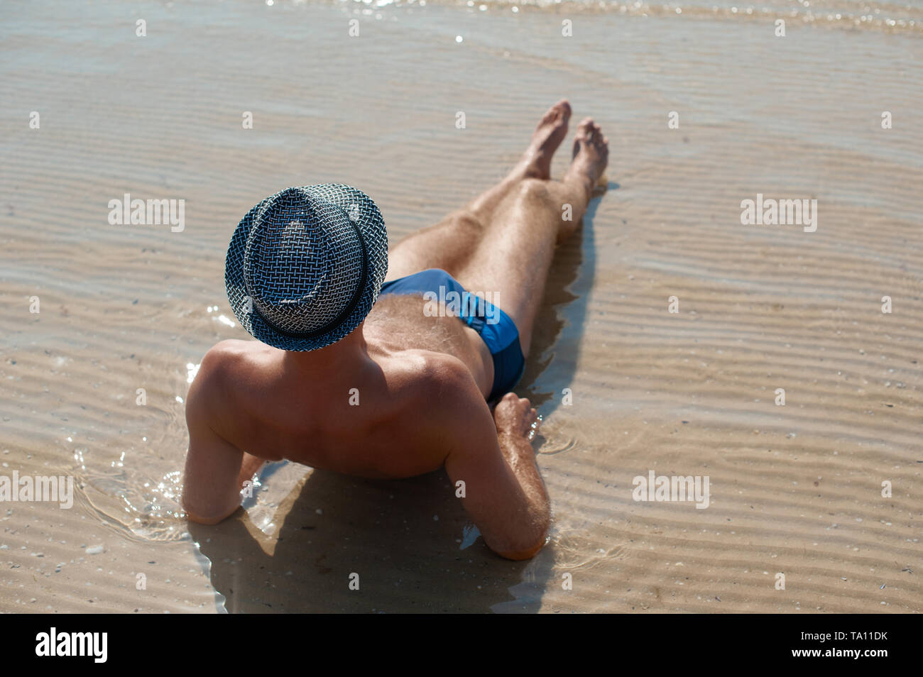 Elegante giovane maschio modello uomo disteso sulla spiaggia di sabbia di indossare hipster estate hat godendo di viaggio estivo vacanza vicino al mare Foto Stock