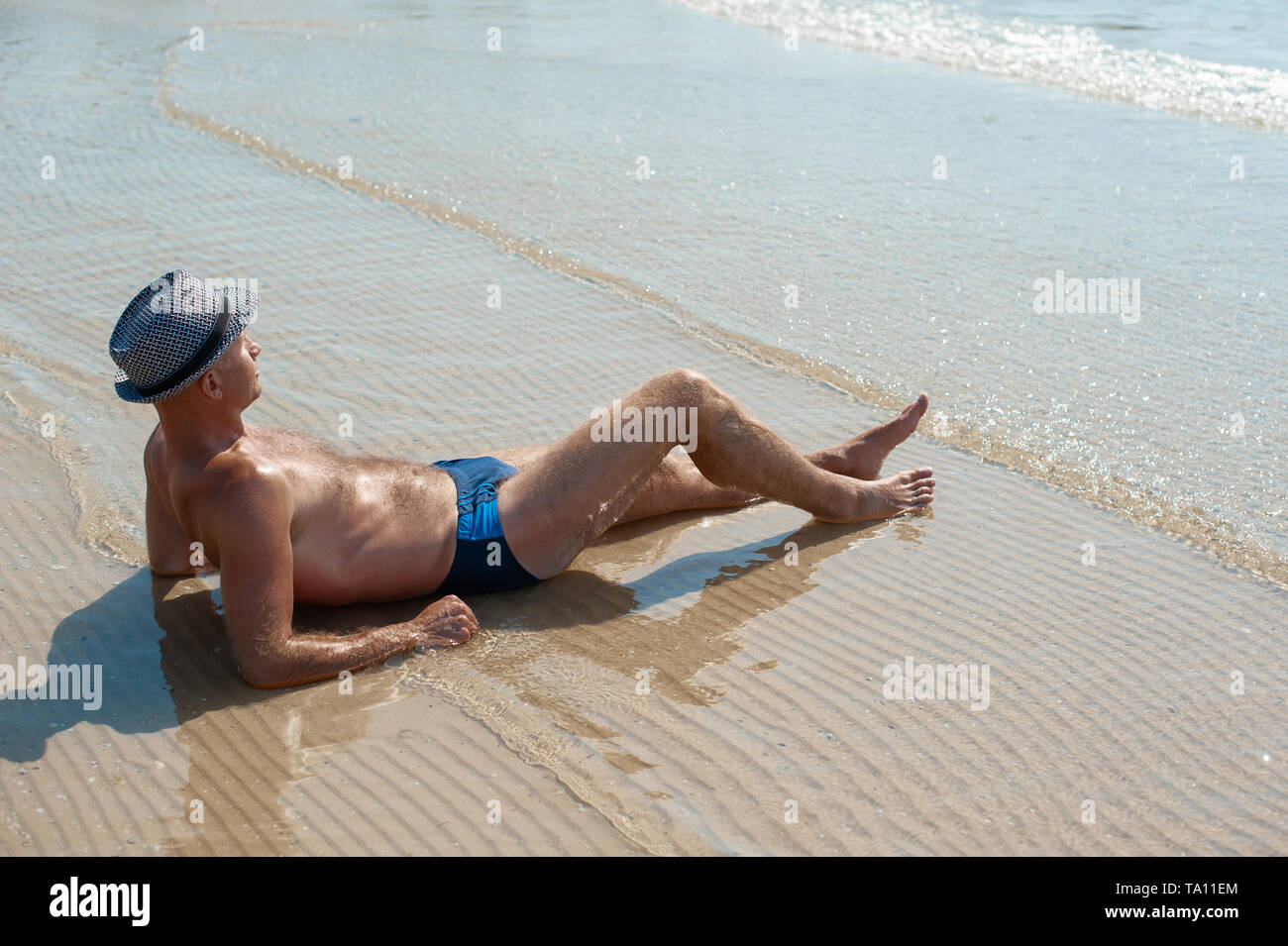 Elegante giovane maschio modello uomo disteso sulla spiaggia di sabbia di indossare hipster estate hat godendo di viaggio estivo vacanza vicino al mare Foto Stock