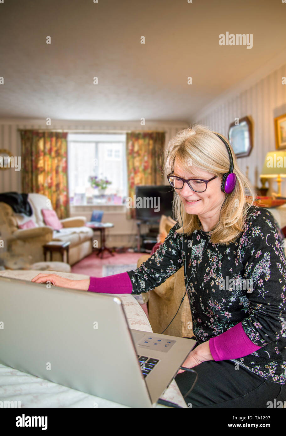 La madre lavora in casa,online con il suo computer a sorridere al suo schermo con divertimento. Foto Stock