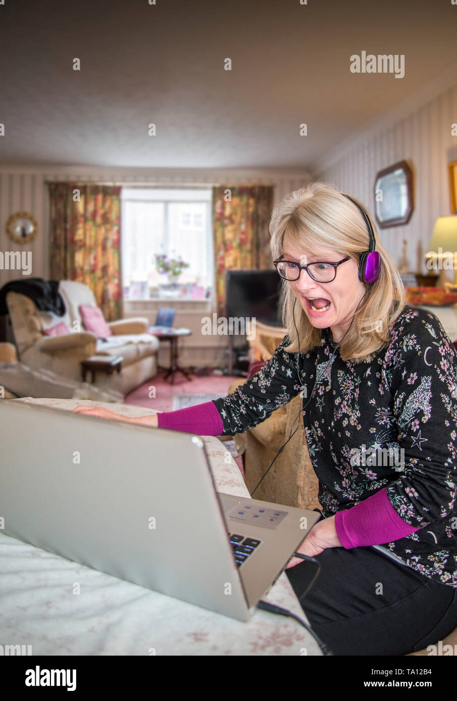 Una madre a casa,online con il suo computer la visualizzazione di forti emozioni a ciò che lei sta vedendo e testimoniando sullo schermo. Foto Stock