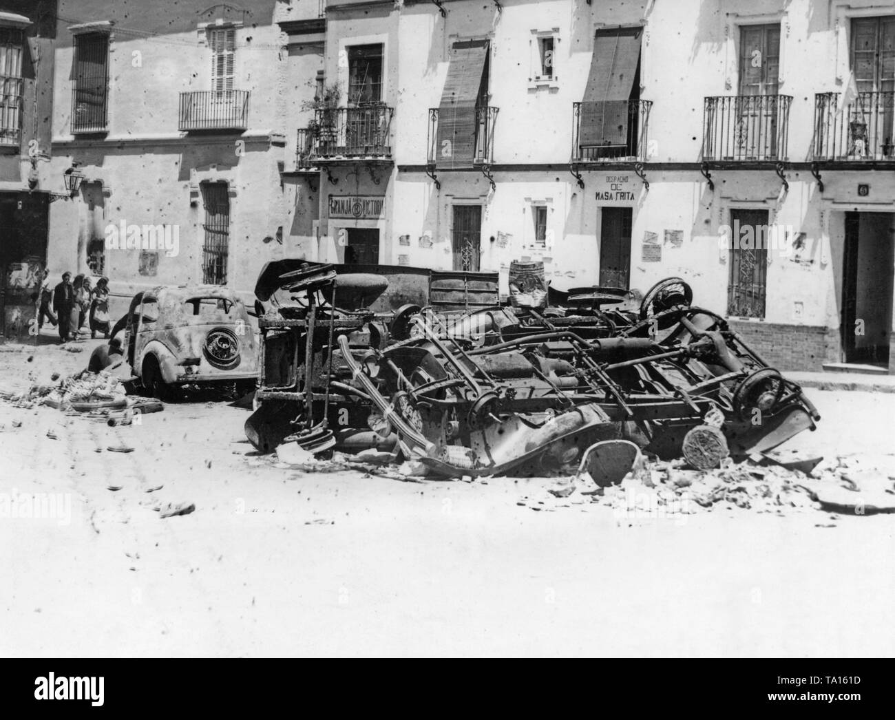 Foto di una strada dopo la conquista delle truppe franchista a Siviglia, in Andalusia, Spagna. In primo piano, è esplosa e bruciate le vetture. Il muro di casa in background è disseminato di proiettili e la mitragliatrice fuoco. Le finestre e le porte sono bloccate. In background, avvicinando i civili. Foto Stock