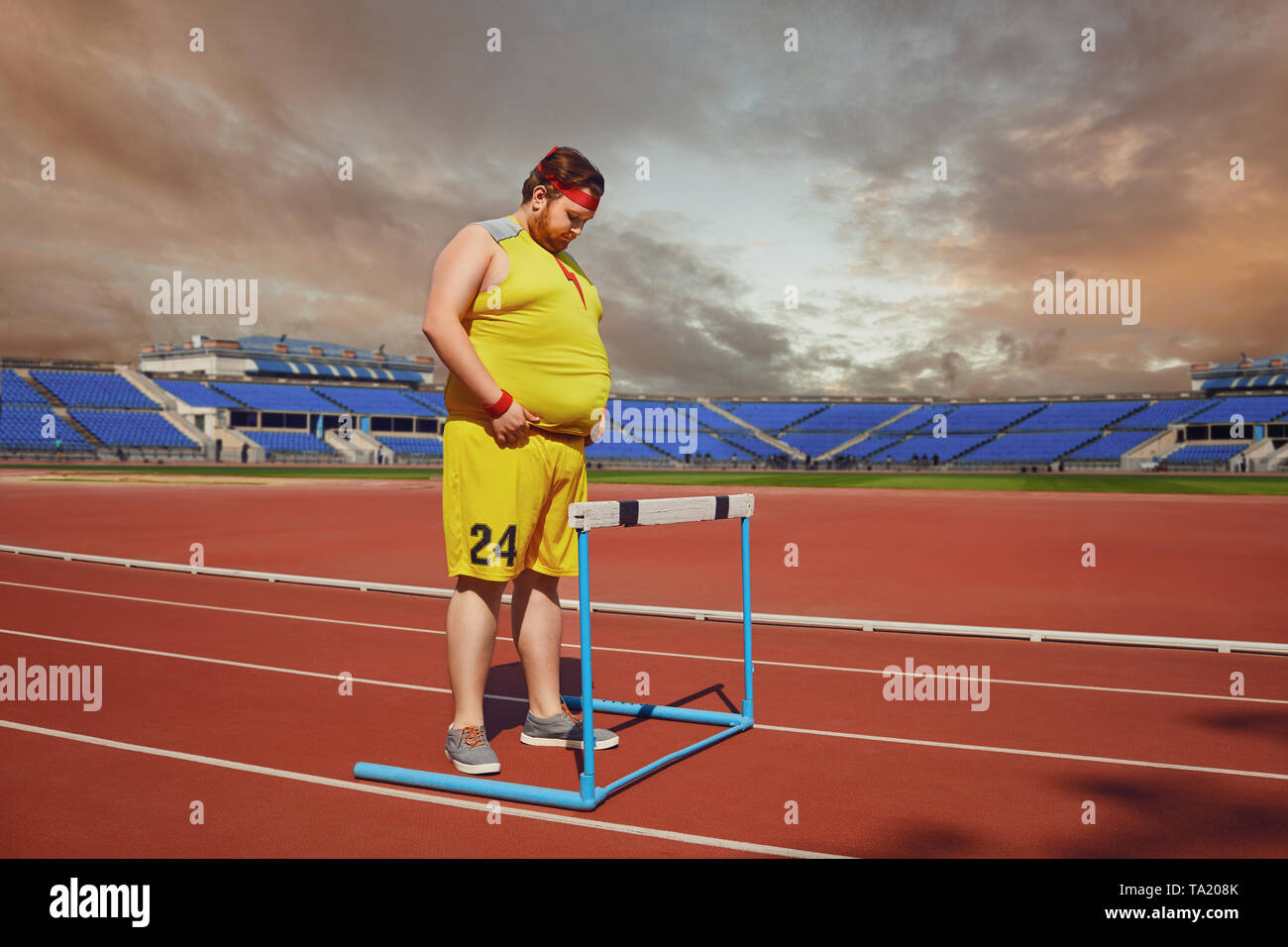 Fat Man in sportswear sta in piedi di fronte ad una barriera su una pista stadium. Vincitore concetto successo ostacolo problema. Foto Stock
