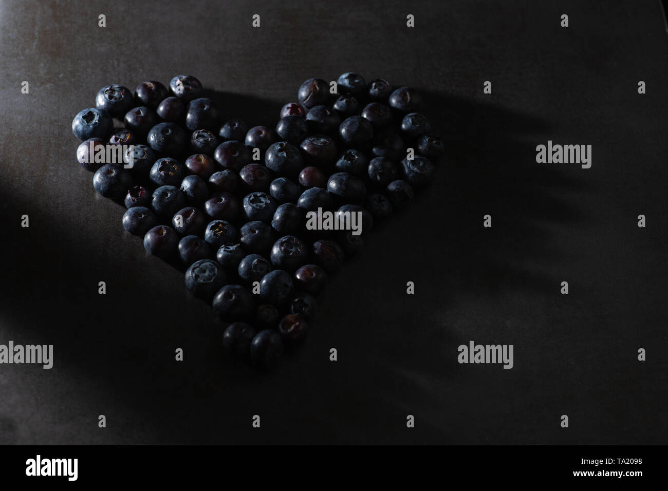 Tasto basso i mirtilli in una forma di cuore. Dark e moody luce intenzionale. Moderno e Contemporaneo ed elegante il cibo sano immagine. Foto Stock