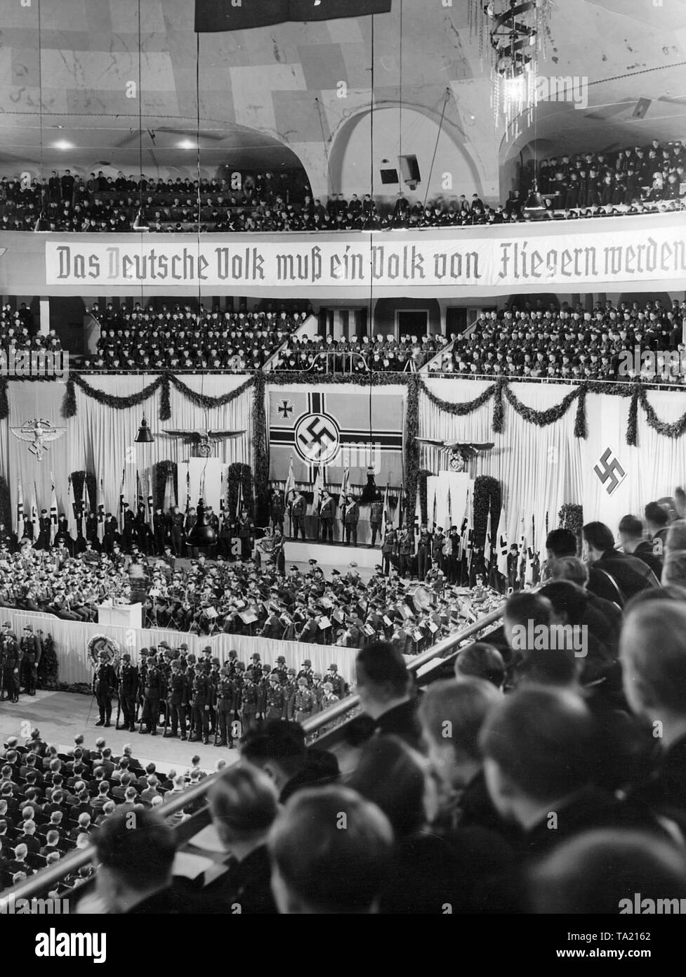 Rally di massa della Air Force. Nazi Air Force Corps e Gioventù Hitleriana in apertura della Settimana di propaganda della Luftwaffe. Sopra il portabandiera di una bandiera della Luftwaffe, sopra il banner leggere 'Dcome deutsche Volk muss ein Volk von Fliegern' (la nazione tedesca deve diventare una nazione di volantini). Foto Stock