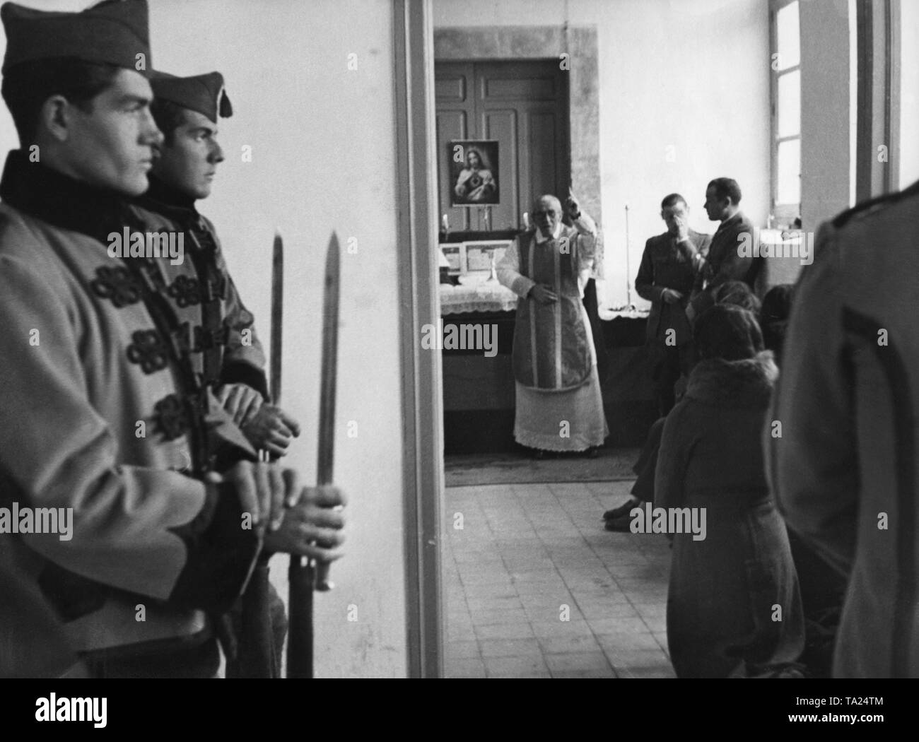 Foto di Cattolica la Messa domenicale per reclute della nazionale spagnola di truppe in una baracca a Salamanca il 16 dicembre 1936. Un sacerdote benedice i soldati davanti all altare e un'immagine di Gesù. Una donna si inginocchia davanti a lui. Due ufficiali stare sulla destra. In primo piano, i soldati in uniforme di parata e baionette a guardia della porta. Foto Stock