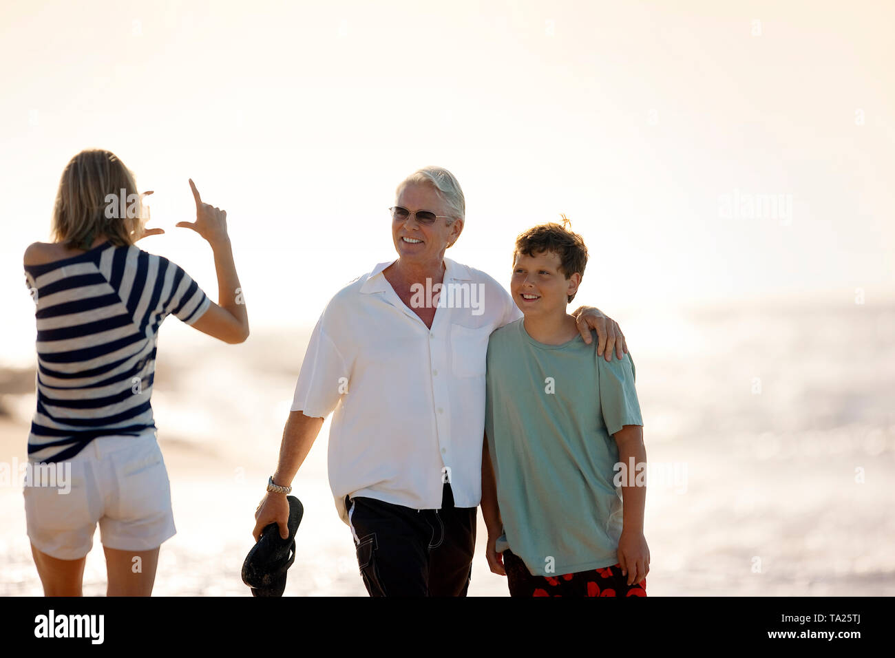 Metà donna adulta fingendo di essere scattato una foto del marito e figlio sulla spiaggia. Foto Stock