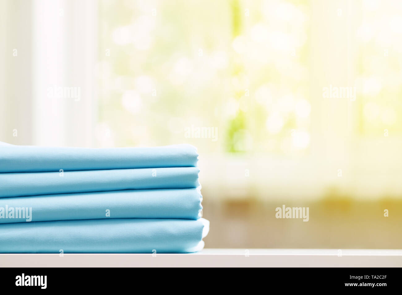 Close-up di blu biancheria da letto pulita su uno sfondo sfocato. Una pila di fogli piegati lenzuola sul tavolo. La luce del sole dalla finestra. Foto Stock