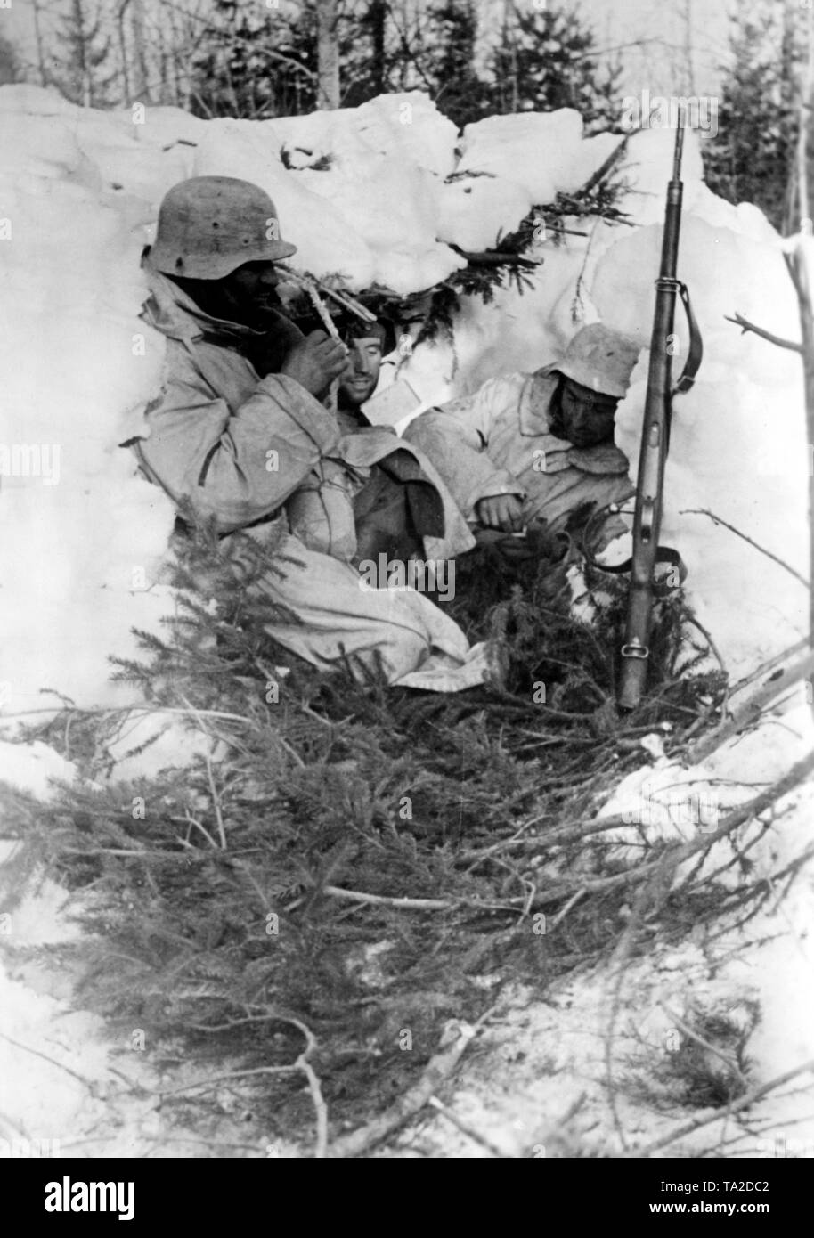 I soldati tedeschi di riposo in una pausa nella lotta dietro una parete di neve. Si proteggono con i rami degli alberi contro la neve. Foto di Propaganda Company (PK): corrispondente di guerra Kraaywanger. Foto Stock