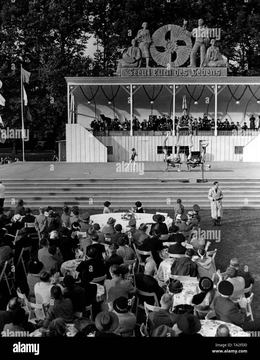 In un festival dell'organizzazione nazista "Kraft duch Freude' ('Sforzo attraverso Gioia") a Treptow, il festival i visitatori vengono intrattenuti con rappresentazioni artistiche, qui una piramide umana. Sullo sfondo di una tribuna con una orchestra di musica. In precedenza, l'emblema della KdF e lo slogan "Freut euch des Lebens' ('Godersi la vita"). Foto Stock