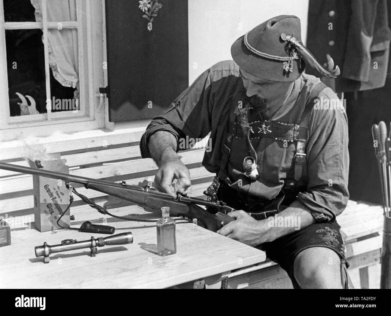 Un cacciatore di fronte al rifugio sul pascolo alpino in Baviera pulisce la sua arma, un fucile a ripetizione del sistema Mauser. Sul tavolo, la portata rimossa, olio di pistola e trainare. Foto Stock