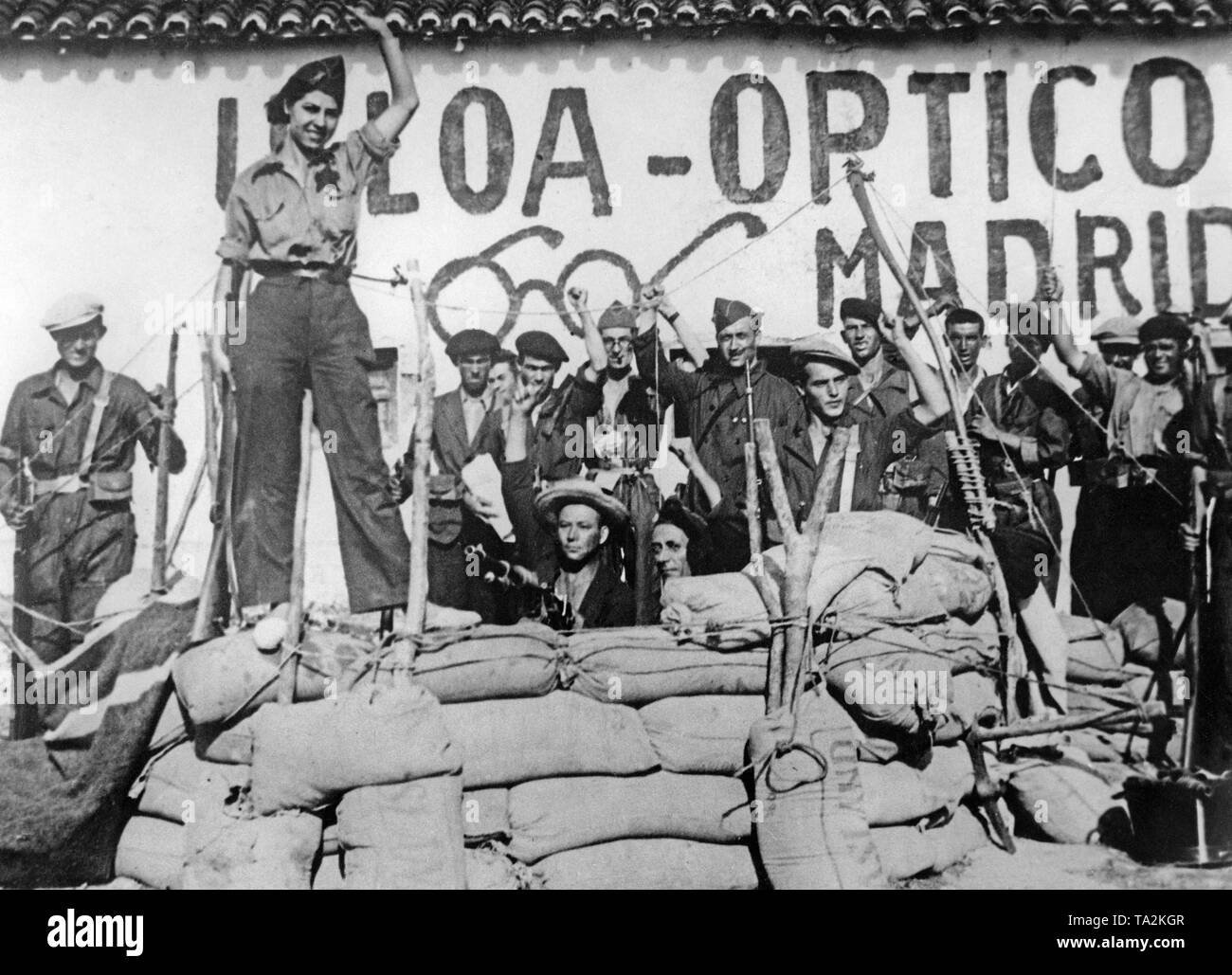 Foto di un gruppo di combattenti repubblicano dietro un contrappeso barriera a Madrid nel mese di agosto 1936. Un combattente donna si erge sulla posizione. In mezzo, una Hotchkiss M1914 mitragliatrice. Sullo sfondo vi sono i combattenti armati con moschettoni alzando il pugno. Dietro la facciata di Ulloa-Optico, un ottico. Foto Stock