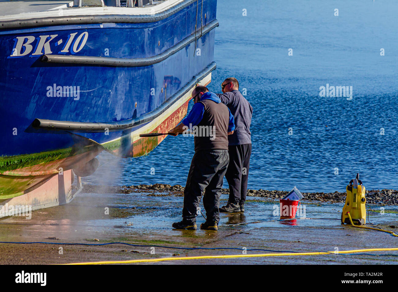 I pescatori spruzzano la loro barca da pesca con una rondella di pressione per rimuovere le alghe dallo scafo. Seahouses, Northumberland, Regno Unito. Ottobre 2018. Foto Stock