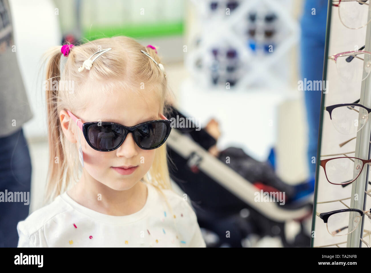 Carino piccola ragazza bionda caucasica giovane che prova sopra e che  sceglie gli occhiali da sole davanti allo specchio al deposito ottico degli  occhiali. Adorabile bambino scolaro avendo Foto stock - Alamy