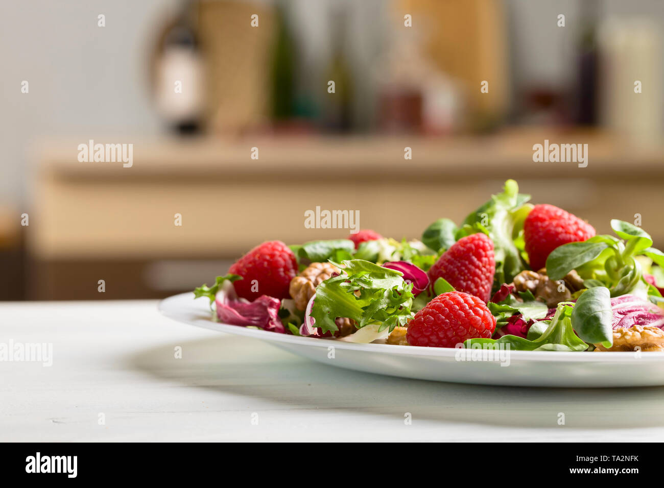 Una sana insalata verde con lampone e noci su una cucina bianca tabella. Foto Stock