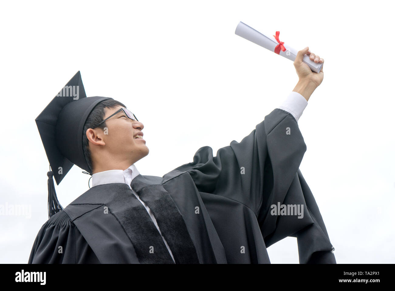 Giovane uomo indossare il cappello e abito vestito di graduazione e tenere il suo certificato Foto Stock