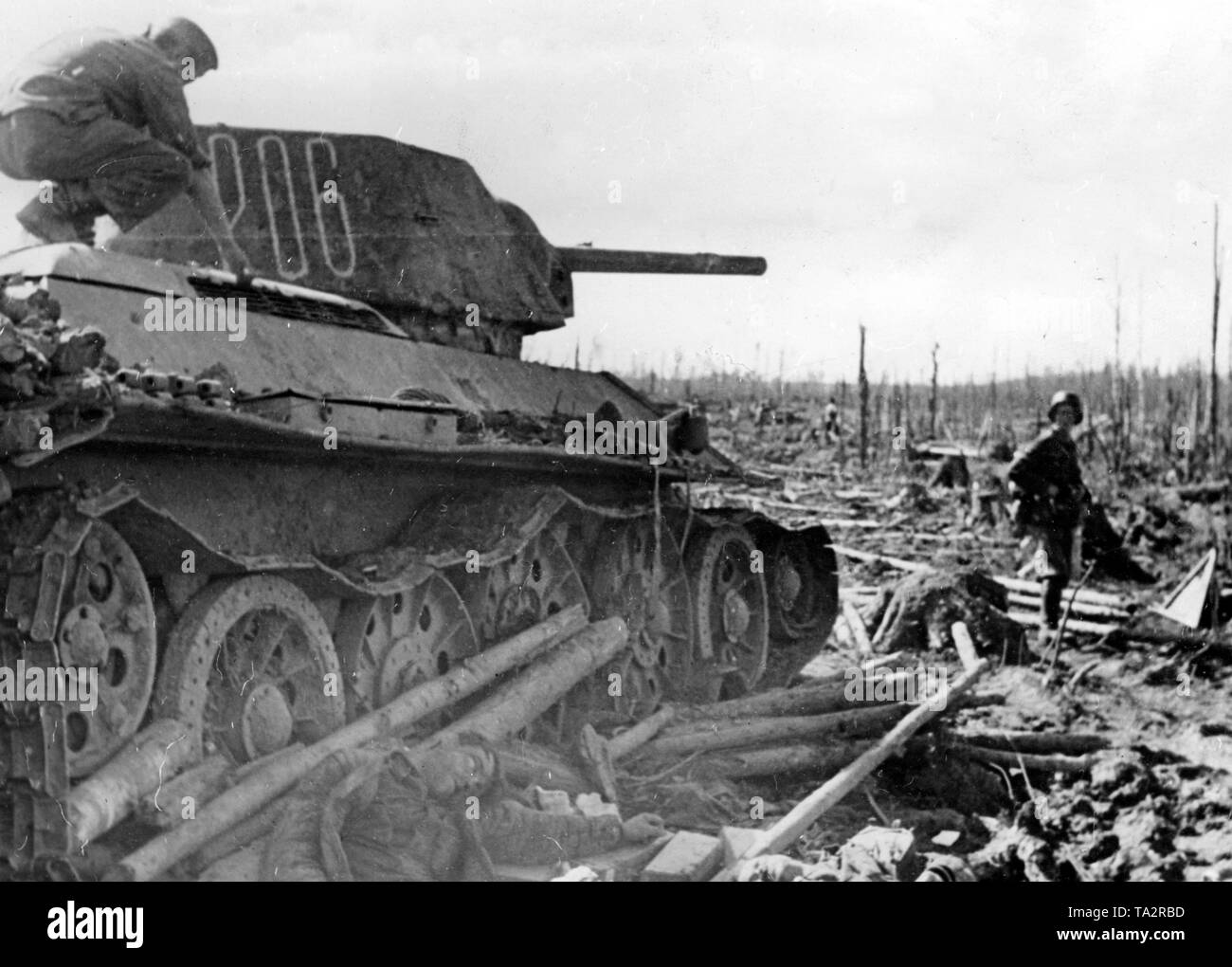Un soldato tedesco si arrampica su un colpo giù T-34 sul fronte Volkhov. Accanto ad esso, un soldato ucciso giacente a terra. Le contese distrutte vaste aree di foresta. Foto di Propaganda Company (PK): corrispondente di guerra Schuerer. Foto Stock