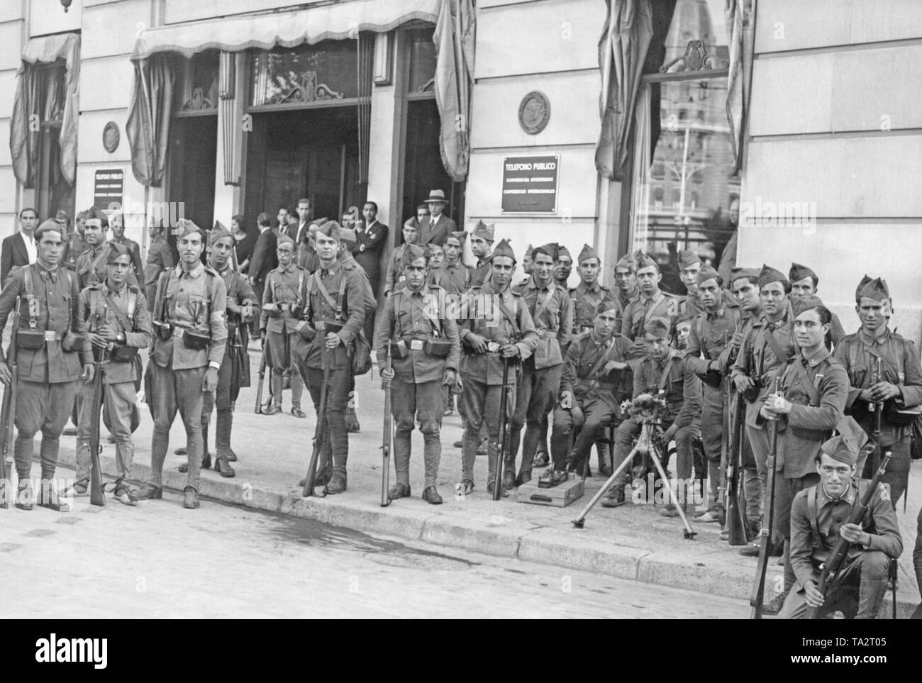 Soldati spagnoli sono in posa armate pesantemente durante il colpo di stato contro la seconda Repubblica spagnola di fronte ad un edificio della società telefonica di stato nel centro di Madrid del luglio 18, 1937. Sulla destra in primo piano un francese Hotchkiss M1914 mitragliatrice su un carrello della pistola. Ci sono dipendenti in background. Foto Stock