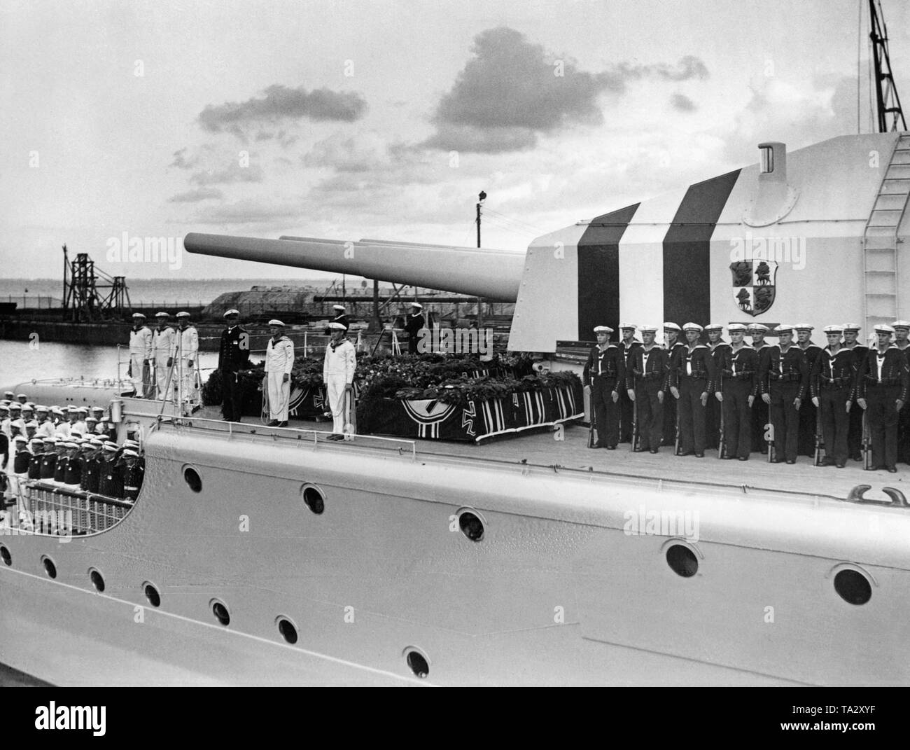 Foto del pianale superiore dell'incrociatore pesante 'Deutschland' con le bare dei suoi membri di equipaggio, che sono stati uccisi nel bombardamento di velivoli repubblicana durante la Guerra Civile Spagnola vicino a Ibiza in giugno 1937, nel porto di Wilhelmshaven nel Mare del Nord. Accanto alle bare adornata con la naval ensign di fiori e ghirlande, la guarnigione ha schierato nel vestire uniformi. Dietro c è la torretta con tre canne di pistola calibro (28cm). Sullo sfondo le installazioni del porto. Foto Stock