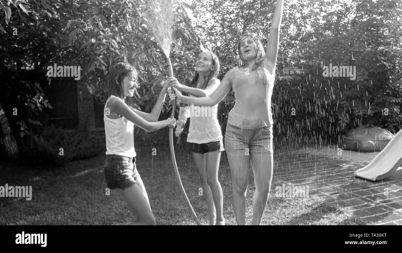 Plack immagine bianco e di allegro ridendo ragazze in vestiti bagnati danzando sotto acqua dal tubo flessibile da giardino in cortile giardino. La famiglia e la riproduzione Foto Stock