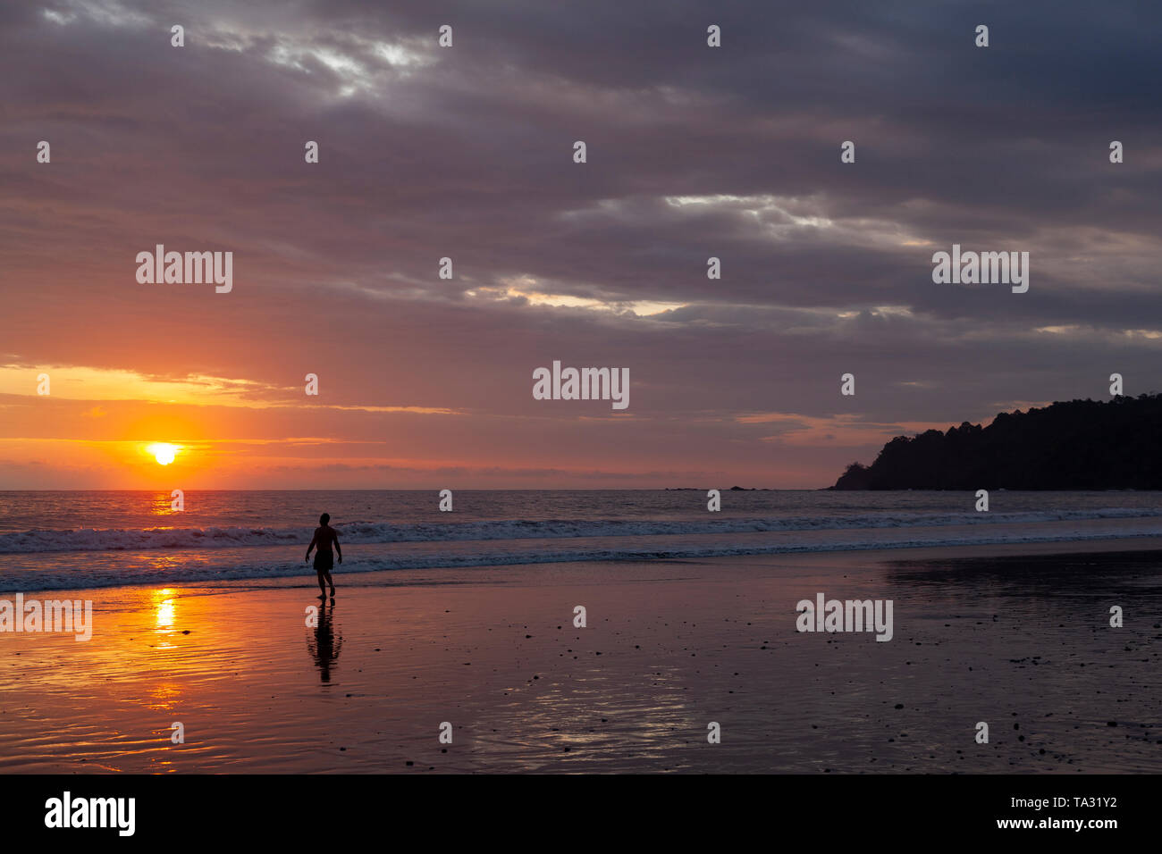 Un uomo a piedi l'acqua sulla spiaggia, tramonto, Playa Espadilla, Parco Nazionale di Manuel Antonio, Costa Rica Foto Stock