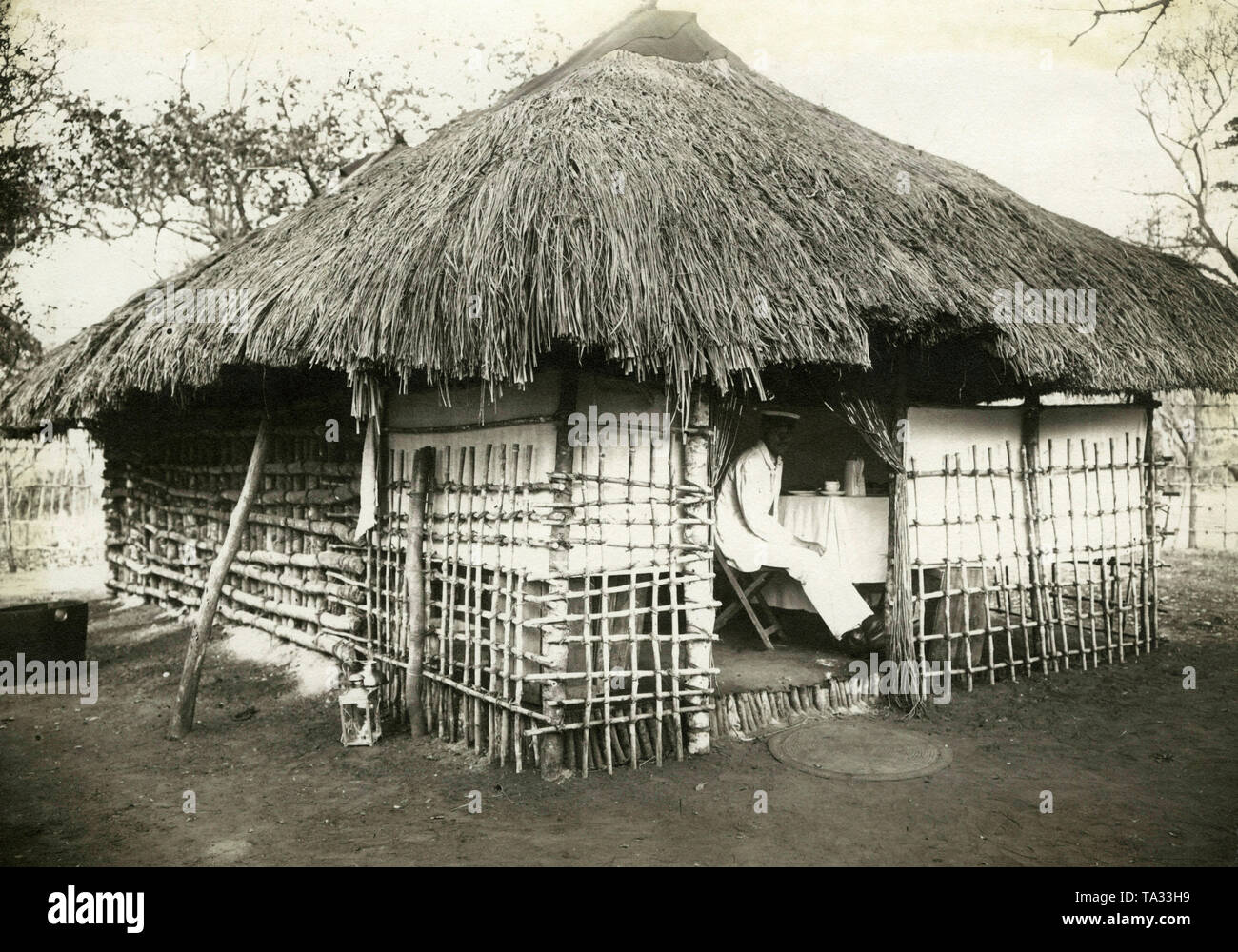 Un uomo bianco, eventualmente un funzionario coloniale, seduti al tavolino in una casa costruita in stile locale nella colonia tedesca di tedesco in Africa orientale. Foto Stock