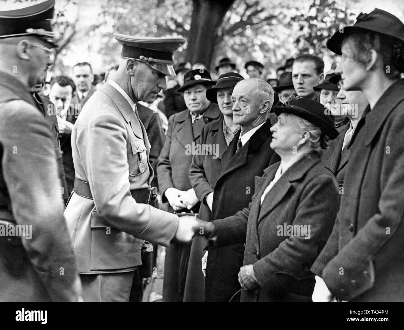Reich Ministro degli Interni Wilhelm Frick (agitando mani) accoglie favorevolmente i parenti di coloro che sono stati uccisi dall'esercito ceco nel 1919 nel cimitero di Kadan il 19 ottobre 1938. Foto Stock