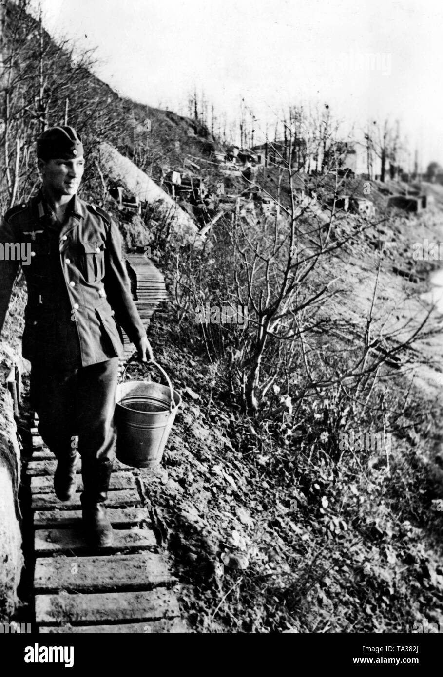 Un soldato tedesco che cammina con una benna lungo un percorso di legno sulla riva meridionale del lago Ilmen. Sul terrapieno, diverse posizioni in tedesco. Foto di Propaganda Company (PK): corrispondente di guerra Muck. Foto Stock