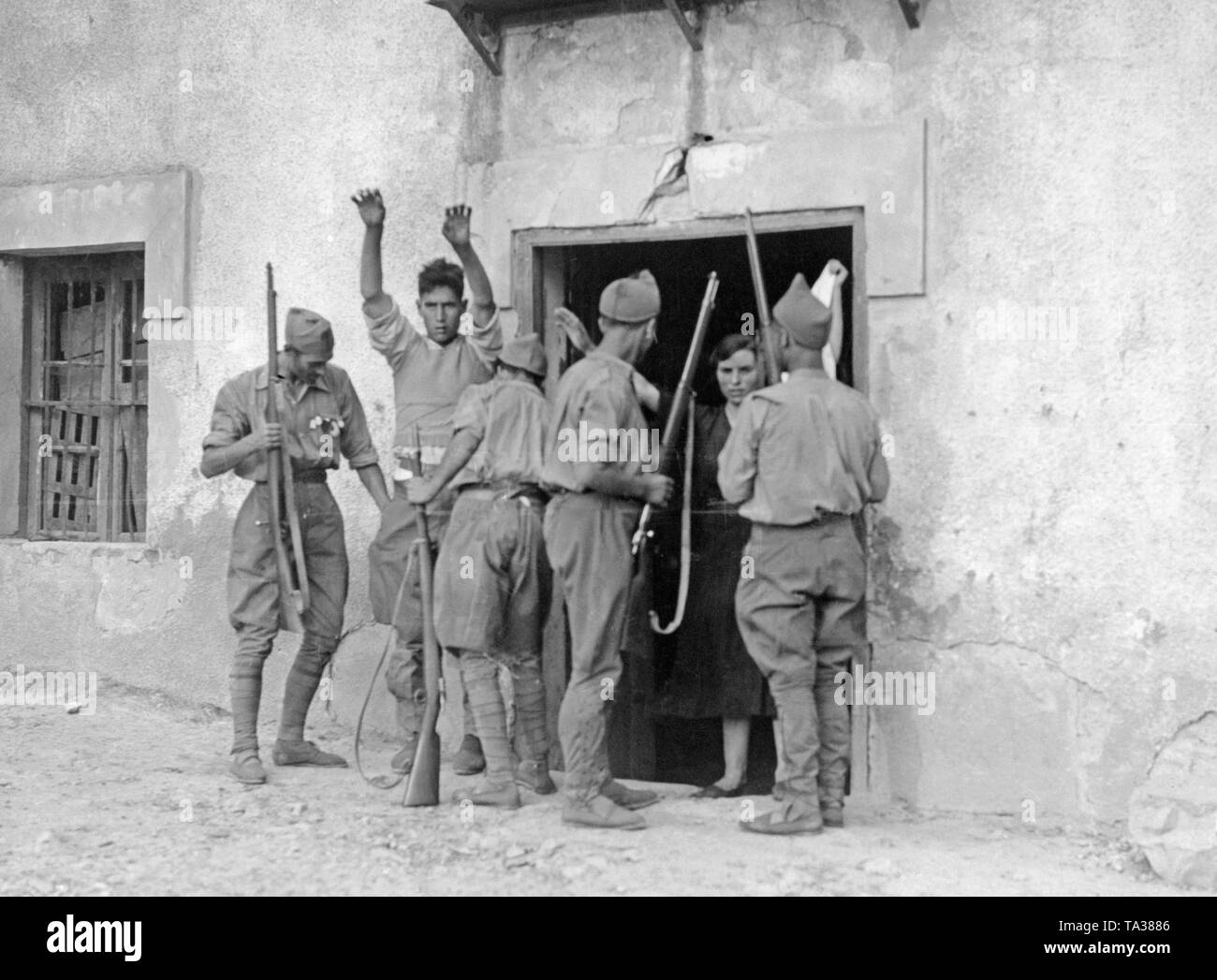 Foto di quattro nazionale spagnolo di soldati nella parte anteriore di una casa colonica in basco di città di confine (Francia) Irun, durante un raid nel settembre 1936. Un uomo e una donna (con un panno bianco) sono esaminate dai soldati per armi nascoste e combattenti repubblicano sono ricercati in casa loro. Foto Stock