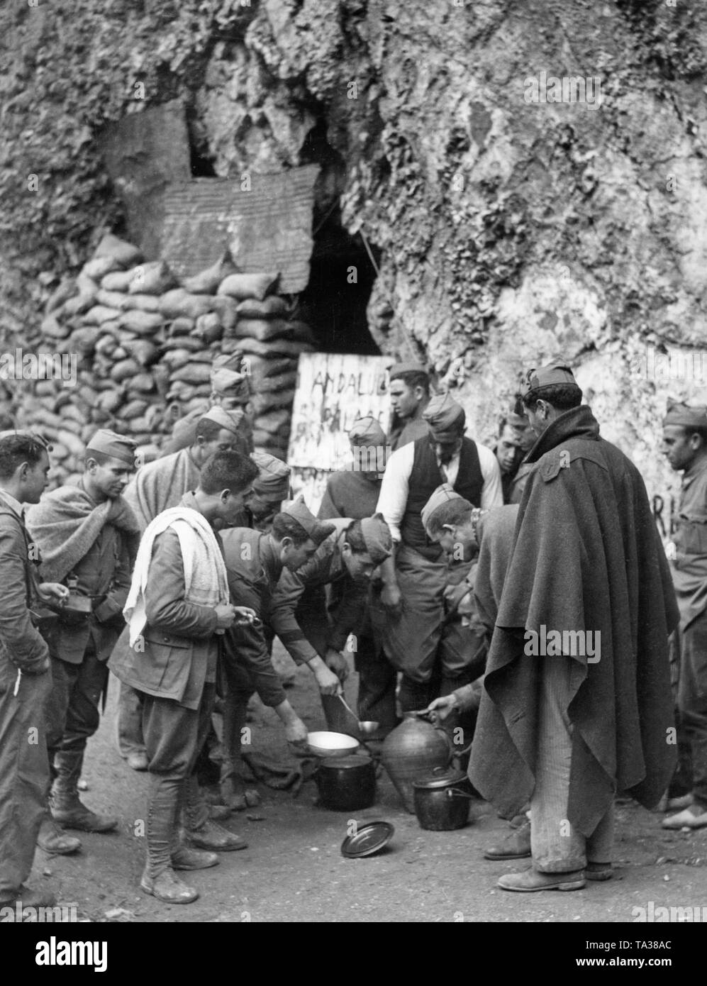 Distribuzione di cibo ai soldati dell'esercito meridionale della nazionale spagnola di truppe nelle montagne della Sierra Nevada, a ovest di Granada, Andalusia nel 1937. In primo piano, gli uomini di mantelli e coperte avvolte con cappucci gorillo mangiare zuppa da pentole. In background, un rifugio protetto con sacchi di sabbia. Foto Stock