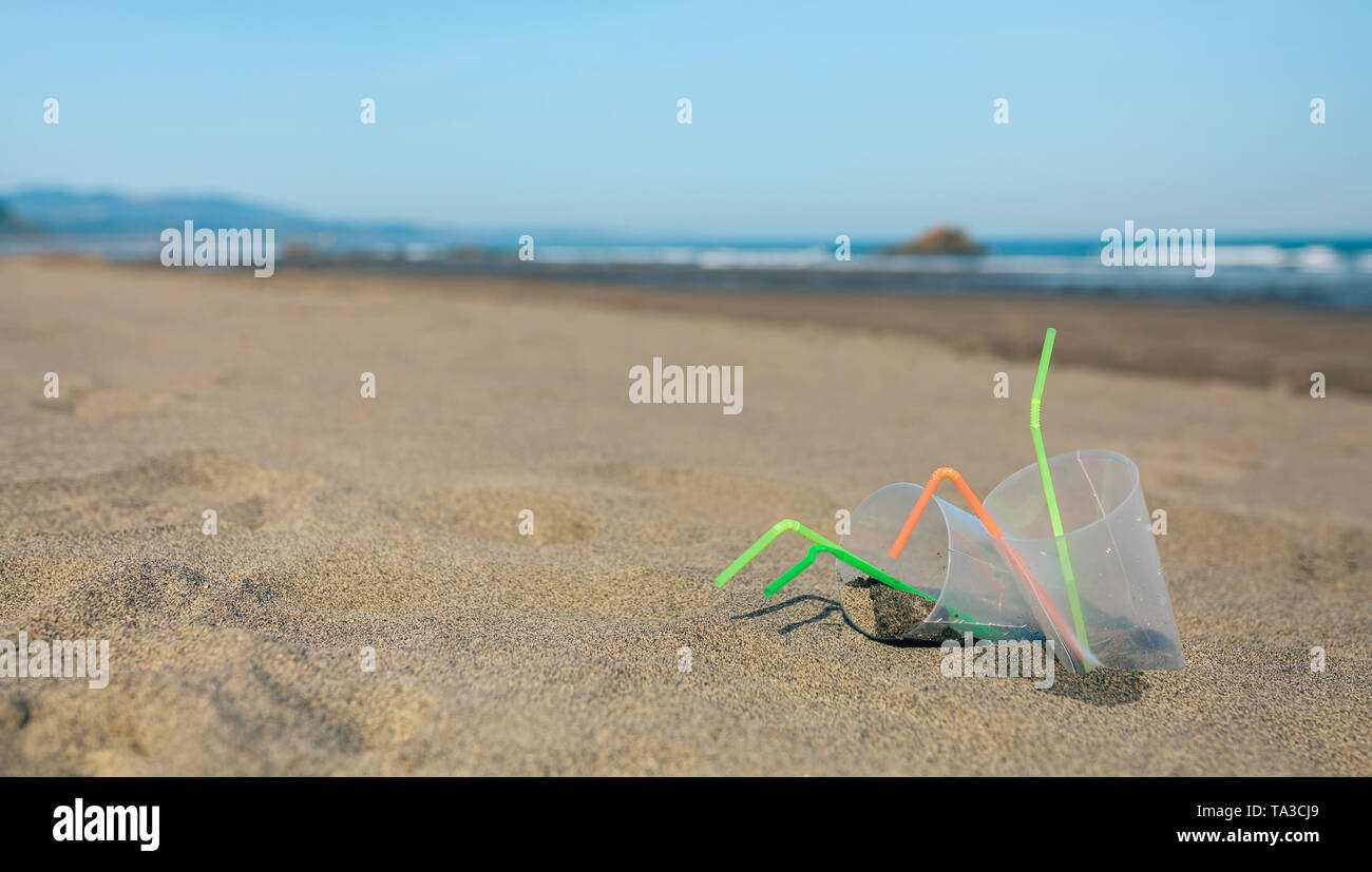 Spiaggia con bicchieri di plastica e cannucce Foto Stock