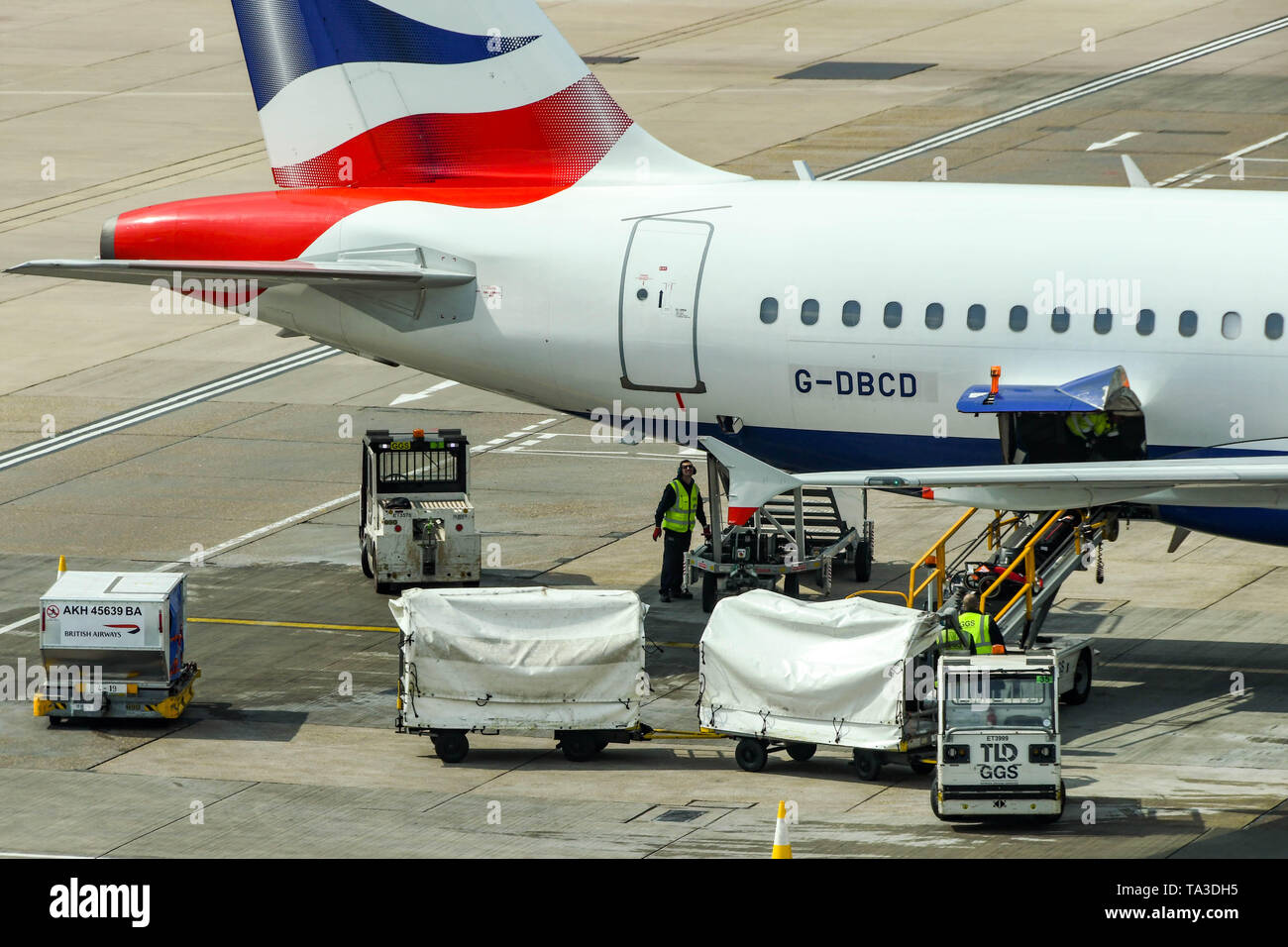 Dall'Aeroporto Gatwick di Londra, Inghilterra - Aprile 2019: i lavoratori con carrelli bagagli valigie di scarico da un British Airways jet presso l'aeroporto di Gatwick Foto Stock