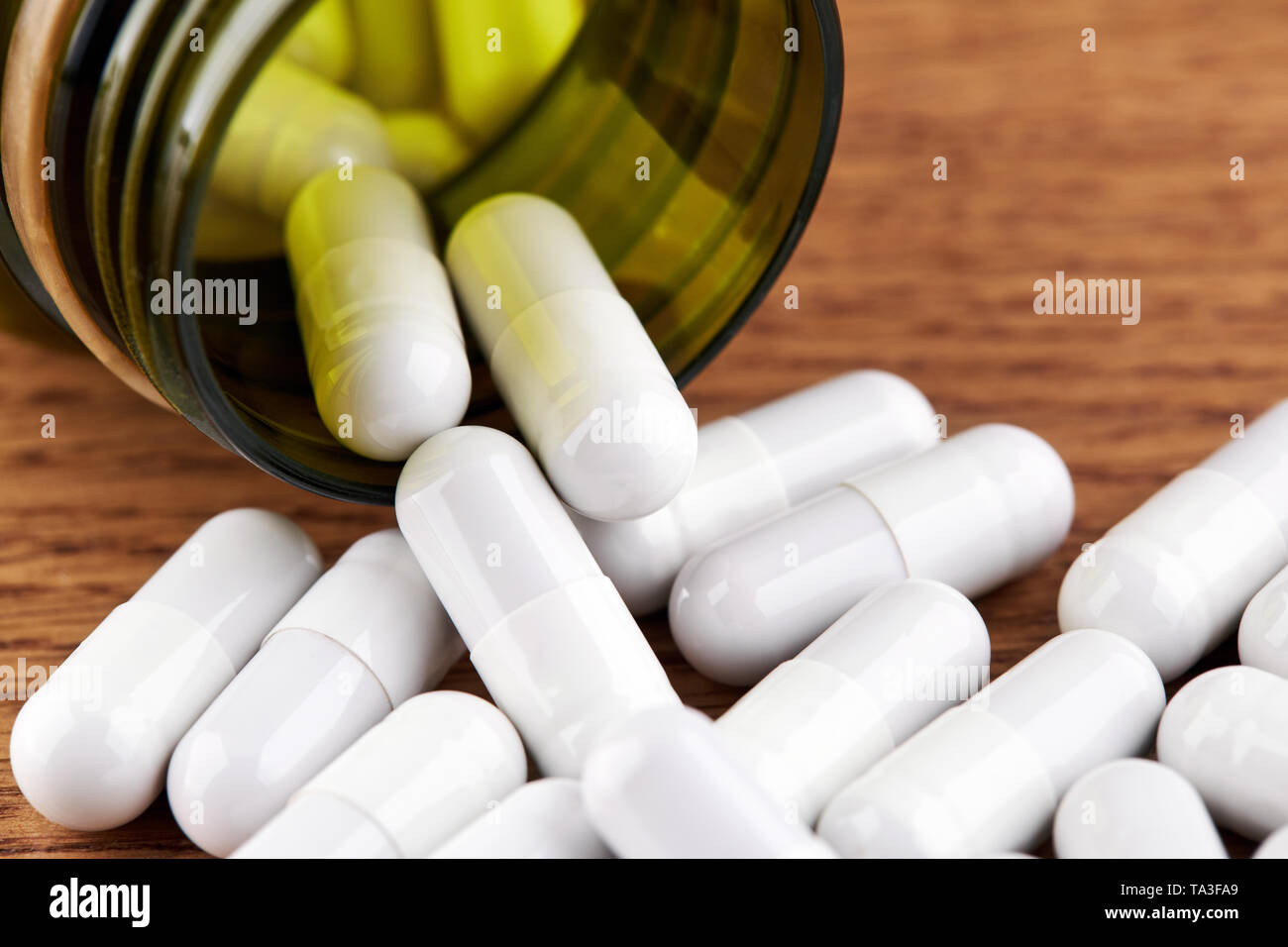 Molte pillole di colore bianco e verde fiala di plastica su sfondo di legno. Foto Stock