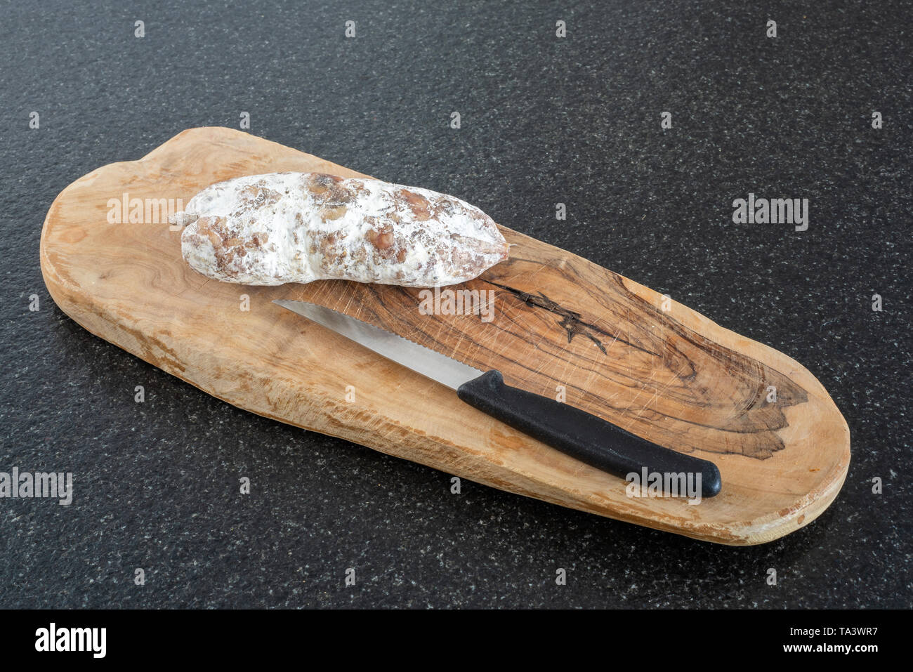 Salsiccia secca e un coltello su legno su una tavola nera vista da vicino Foto Stock