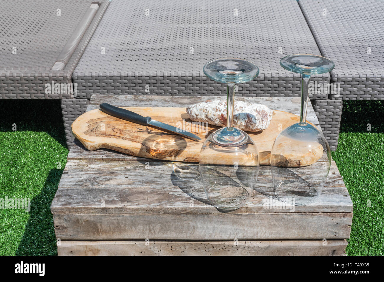 Vuoto due bicchieri di vino e una salsiccia secca con un coltello su un tavolo di legno in un giardino in una giornata di sole Foto Stock