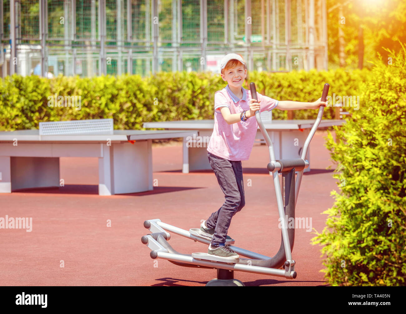 Sorridente ragazzino sullo sport terra esercizio in palestra macchina - capretto felice formazione piedi e braccia in park - bambino divertirsi nella natura Foto Stock
